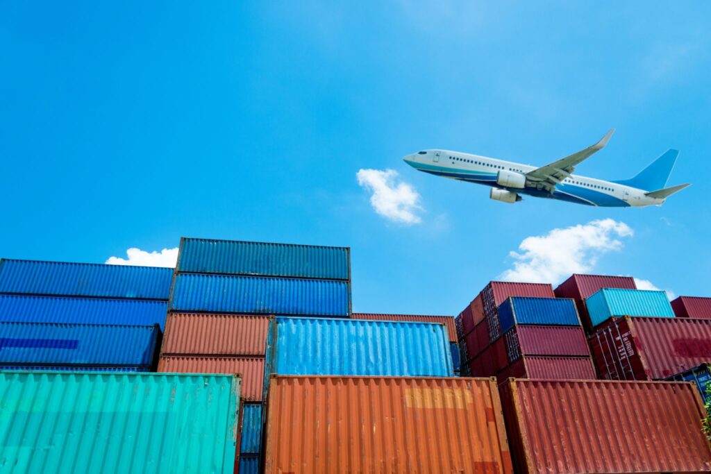 Stacked shipping containers with a cargo plane overhead, representing freight capacity planning for peak season